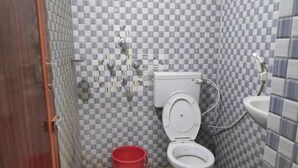 A small bathroom with a toilet, a red bucket, and tiled walls.