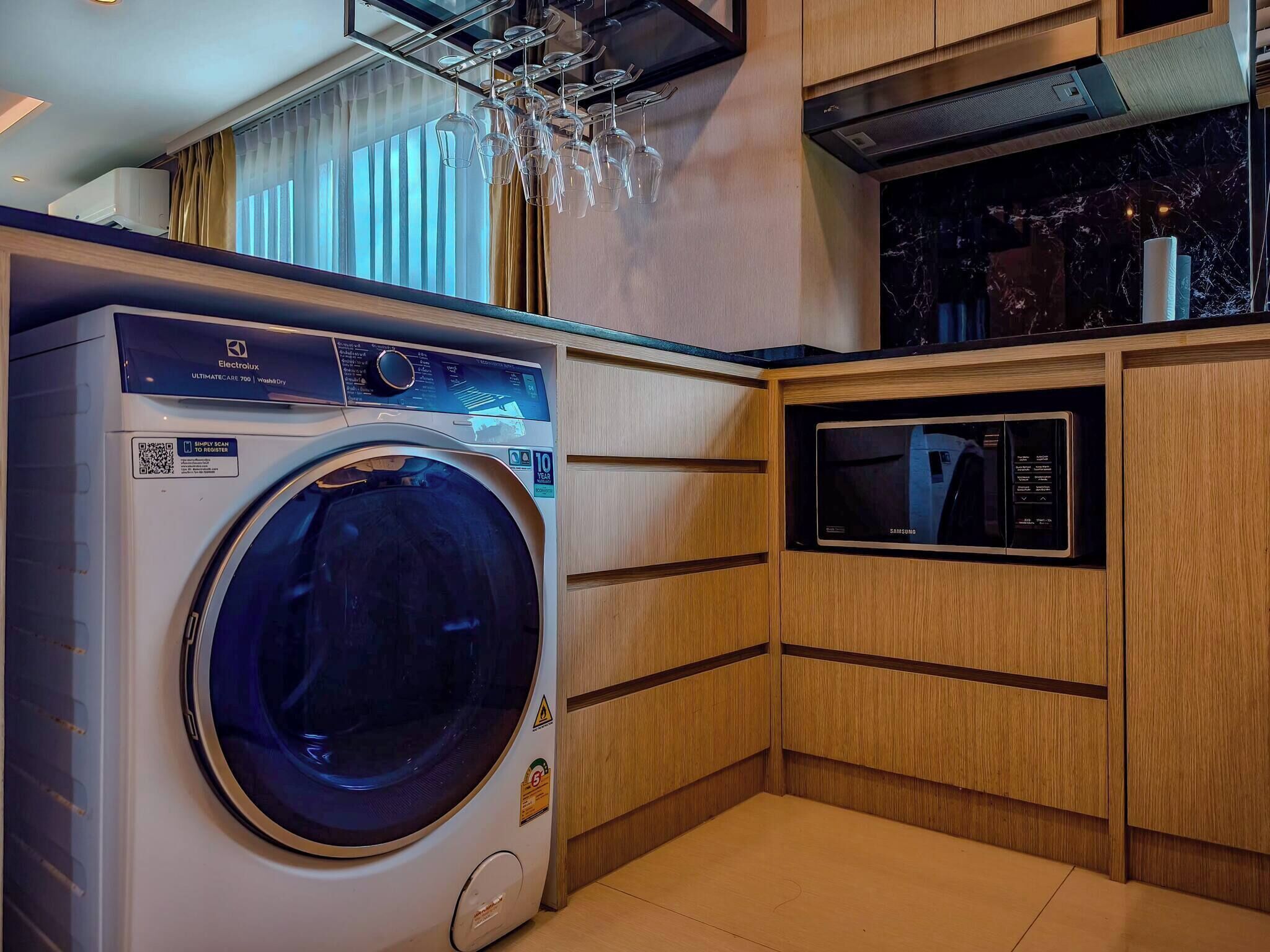 A compact kitchen with a washing machine, a microwave, and wooden cabinetry.
