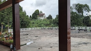 Área externa de concreto com cerca branca, plantas em vasos e um edifício ao fundo.