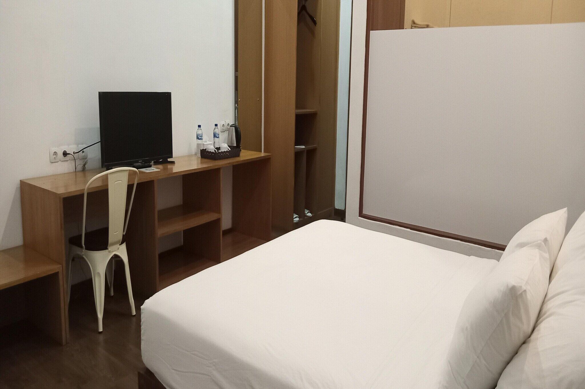 A hotel room with a bed, a desk with a computer, a chair, and a wardrobe.