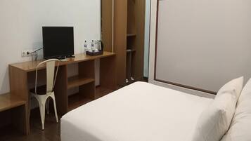 A hotel room with a bed, a desk with a computer, a chair, and a wardrobe.