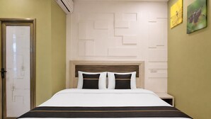 A hotel room with a bed, a nightstand, a wall-mounted air conditioner, and a door with a geometric design.