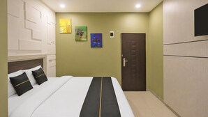 Hotellihuone, jossa on sänky, ovi ja seinälle kiinnitetty taideteos.