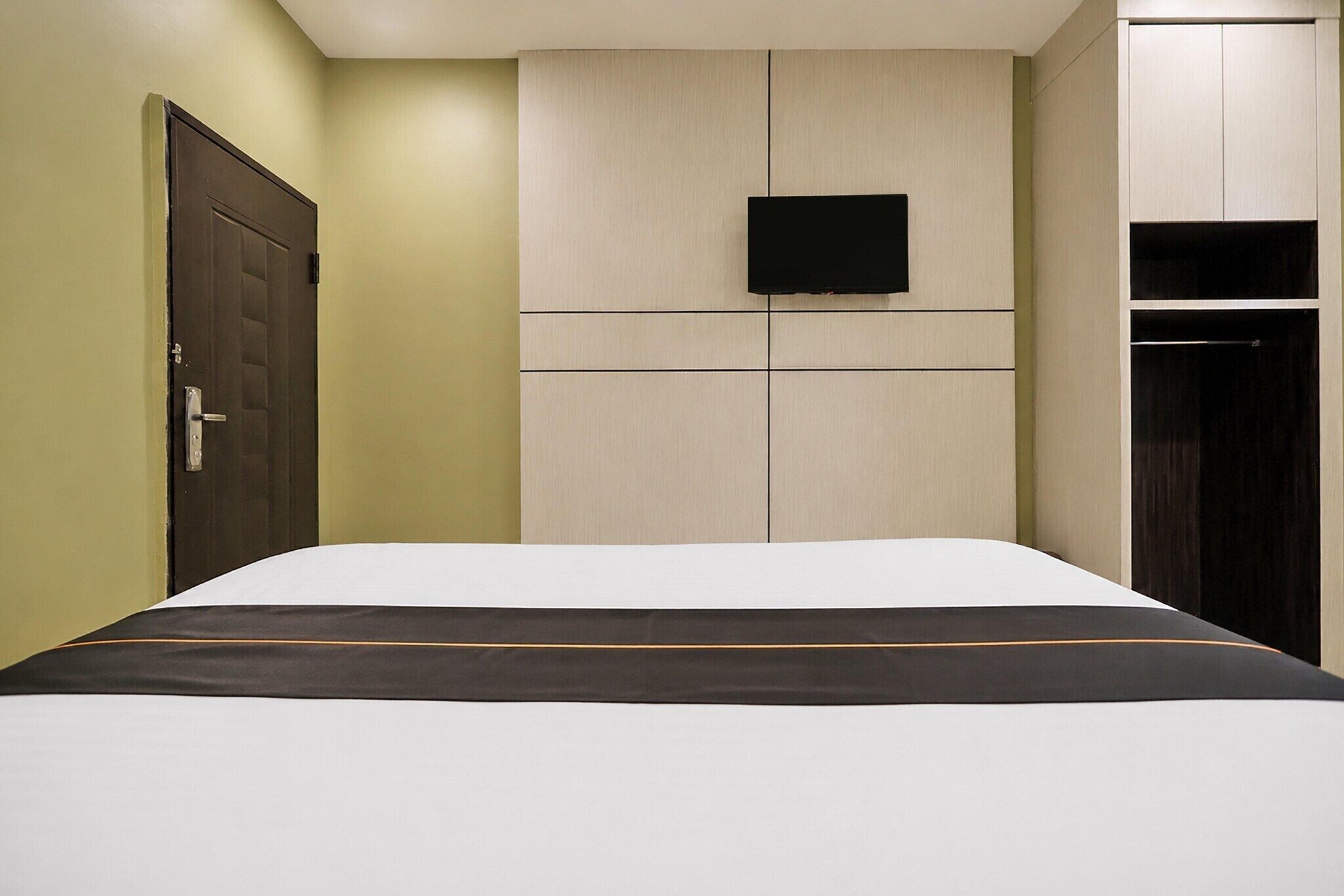 A bedroom with a bed, a door, a wall-mounted TV, and a wardrobe.