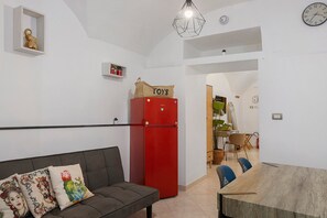 Een moderne woonruimte met een bank, een rode koelkast, een eettafel en een keukenhoek.