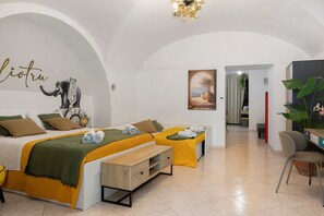Ein Hotelzimmer mit einem Bett, einem Schreibtisch und einem Sessel. An der Wand hängt ein Bild und auf dem Schreibtisch steht eine Pflanze.