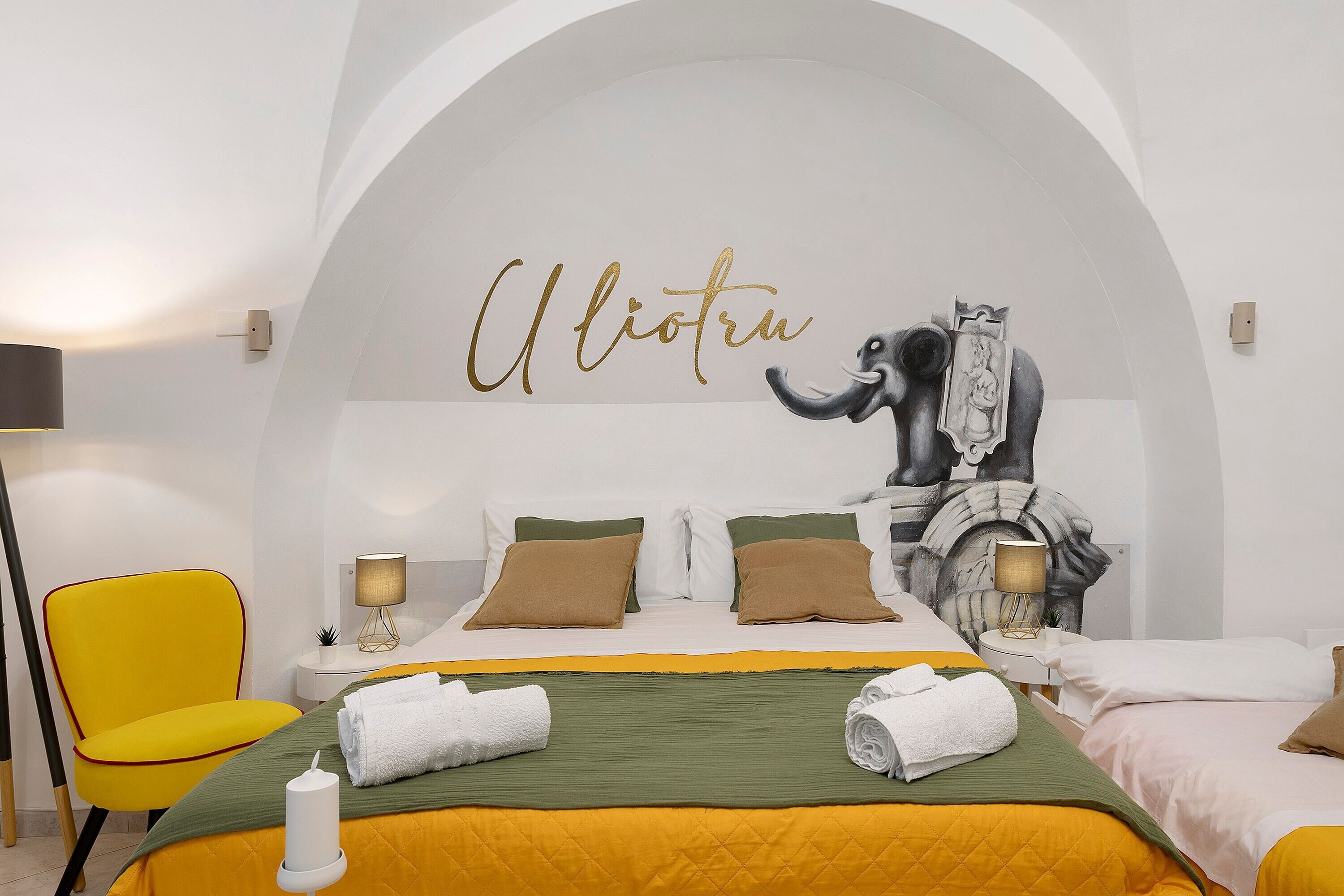 A hotel room with a bed, two pillows, a bedside lamp, a chair, and a wall with a mural.