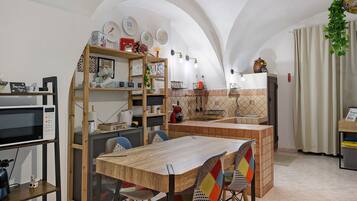 A compact kitchen with a dining area, featuring a wooden table, chairs, and a hanging plant.