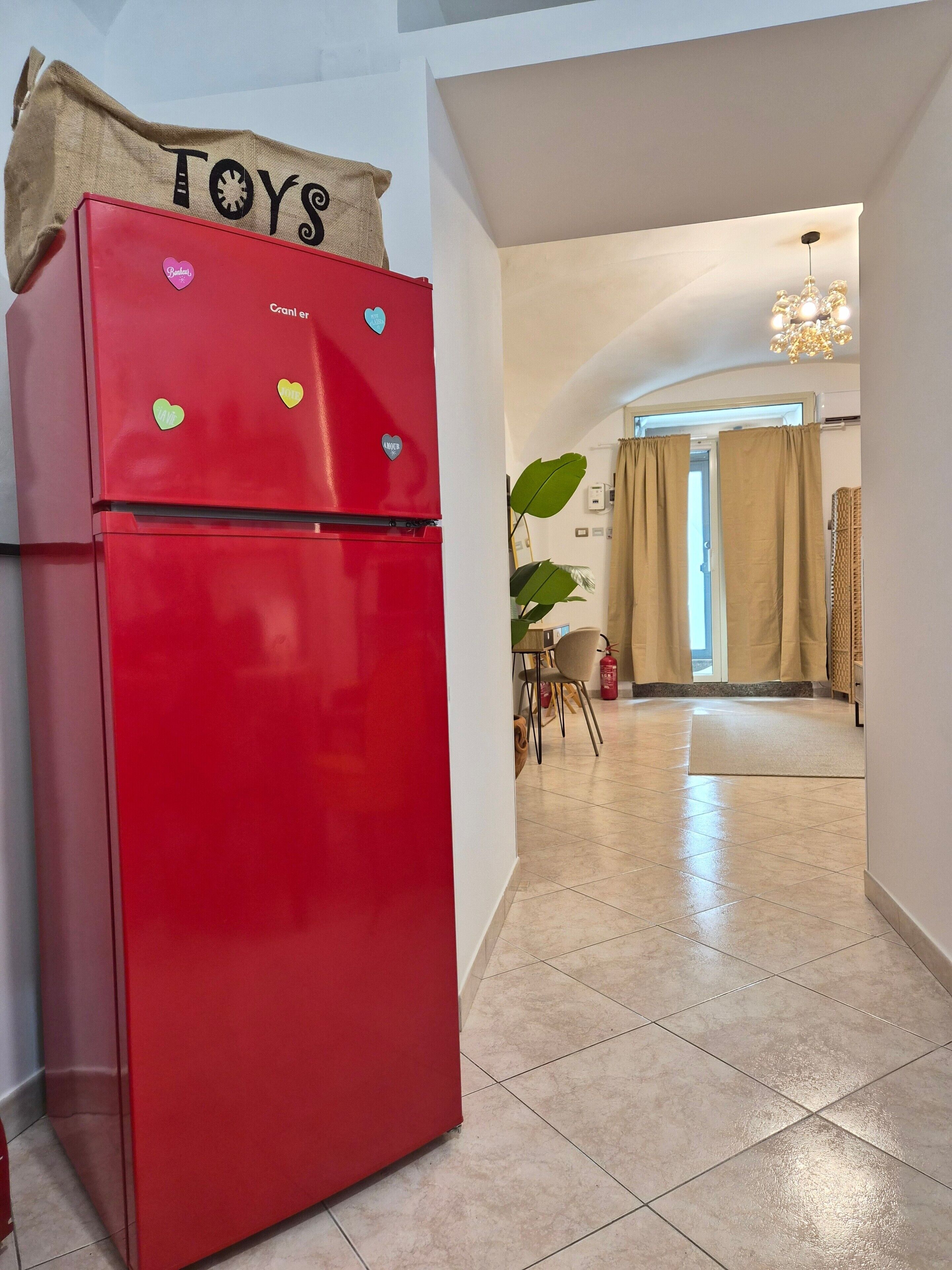 Un réfrigérateur rouge orné d’aimants en forme de cœur et sur lequel est accrochée une pancarte indiquant « JOUETS ».