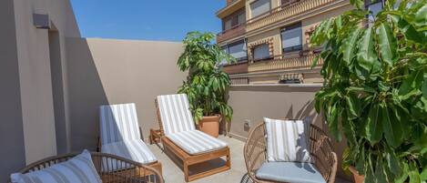 Un balcon agrémenté de meubles en osier, de plantes en pot et offrant une vue sur un immeuble doté de balcons.