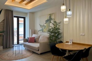 Ein modernes Wohnzimmer mit Sofa, Esstisch mit Stühlen, einer Topfpflanze und einem großen abstrakten Gemälde an der Wand.