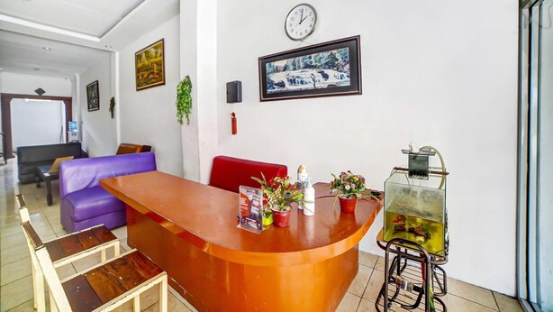 Uma área de recepção com um balcão de madeira, um relógio, uma moldura com imagem e um vaso de planta.