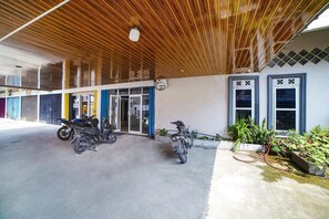 A building with a covered entrance, two motorcycles parked outside, and a garden area with plants and a hose. - Hotel O Brayan | Cozy Single Room (Medan)
