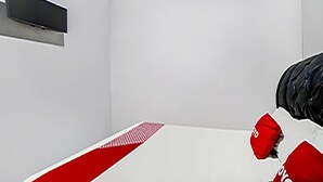 Quarto minimalista com uma cama, uma televisão de tela plana na parede e um cobreleira de cama com padrão vermelho e branco.