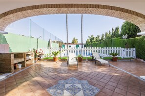 A covered patio area with a tiled floor, a white fence, and a pool in the background. - A&N Diamante, Valle Niza (Benajarafe)