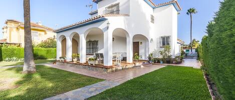 Un edificio blanco con techo de tejas, múltiples arcos y un patio empedrado con plantas en macetas.