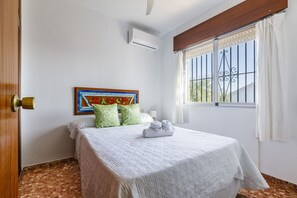 A hotel room with a bed, a window with curtains, a wall-mounted air conditioner, and a door with a brass handle. - A&N Diamante, Valle Niza (Benajarafe)