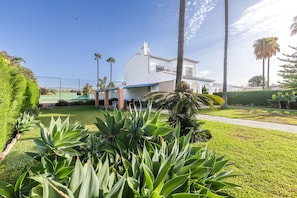 Ein Wohnhaus mit weißem Anstrich, einem Tennisplatz und einem gepflegten Garten mit Agaven.