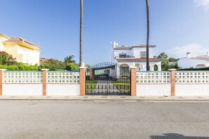 A gated entrance with a white fence and a black gate, leading to a white house with a tiled roof. - A&N Diamante, Valle Niza (Benajarafe)