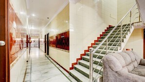Un pasillo de hotel con piso de mármol, una escalera con escalones rojos y verdes, y un sofá mullido.