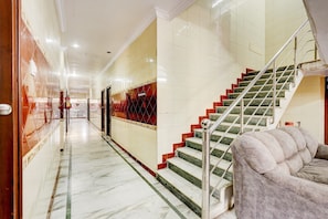 Un pasillo de hotel con piso de mármol, una escalera con escalones rojos y verdes, y un sofá mullido.