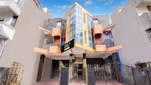 Un edificio moderno con fachada de vidrio destacada, un letrero que indica que es un complejo de departamentos con servicios, y una entrada portón con detalles ornamentales de metal.
