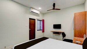 Habitación de hotel con cama, escritorio con silla, televisor, aire acondicionado y armario.
