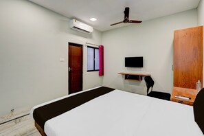 Habitación de hotel con cama, escritorio con silla, televisor, aire acondicionado y armario.