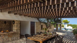 An outdoor patio with a wooden table and wicker chairs, stone walls, and a pergola structure. - Villa MAR DE LUR by Abahana Villas (Calpe / Calp)