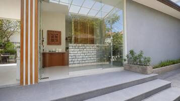 A modern entrance with a glass door, a brick wall, and a small outdoor seating area with a table and chairs.