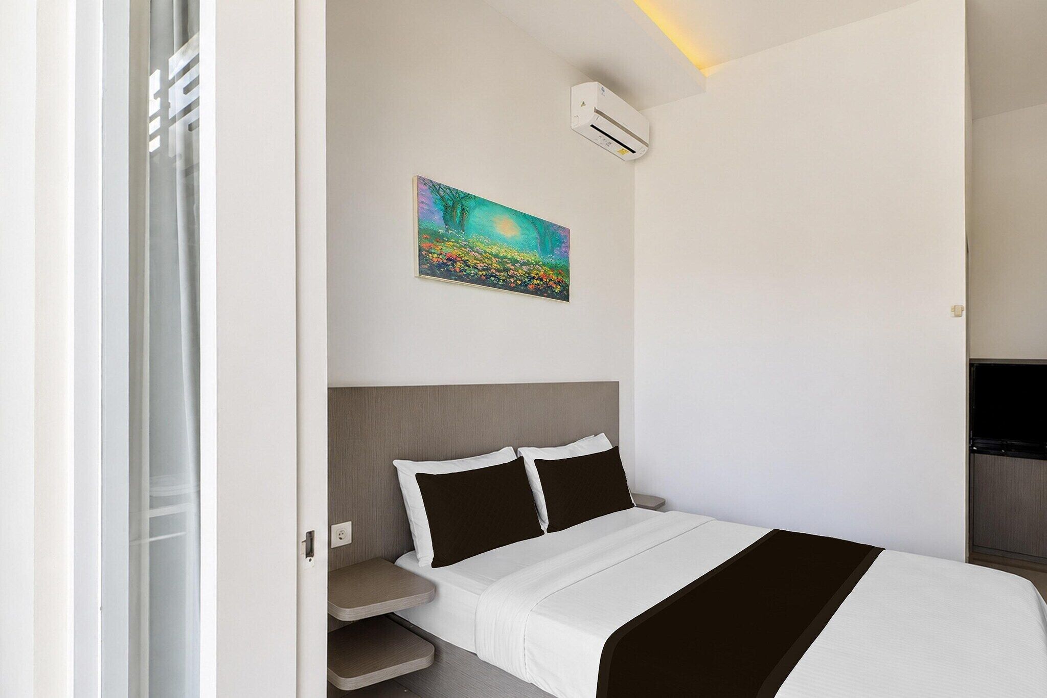 A hotel room with a bed, a painting, an air conditioning unit, and a television.
