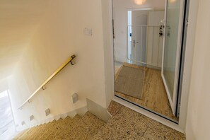 Eine Treppe mit Handlauf, eine Glastür zu einem Duschbereich und eine strukturierte Matte auf dem Boden.