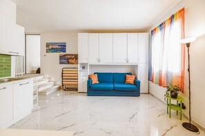 A compact living space with a kitchenette, a blue sofa, a radiator, and a window with curtains. - Sofia's Holiday Room (Tricase)