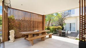 A modern outdoor patio with a wooden table and benches, surrounded by a wooden fence and a view of a building. - Pool Access Suite at The Vinhill Studio (Bali)