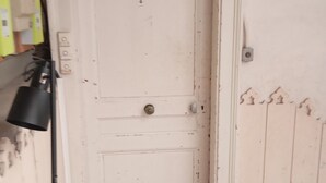 A narrow hallway with a white door, a light switch, and a power outlet on the wall.