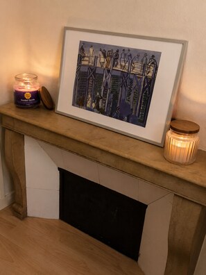 A framed artwork on a mantelpiece, a lit candle, and a jar of scented candle.