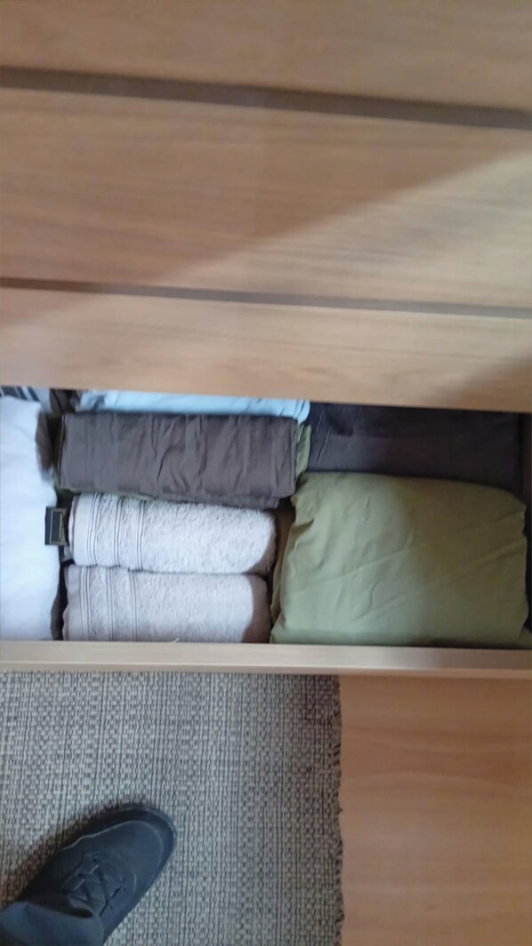 A drawer with folded clothes and a pair of shoes on a textured mat.