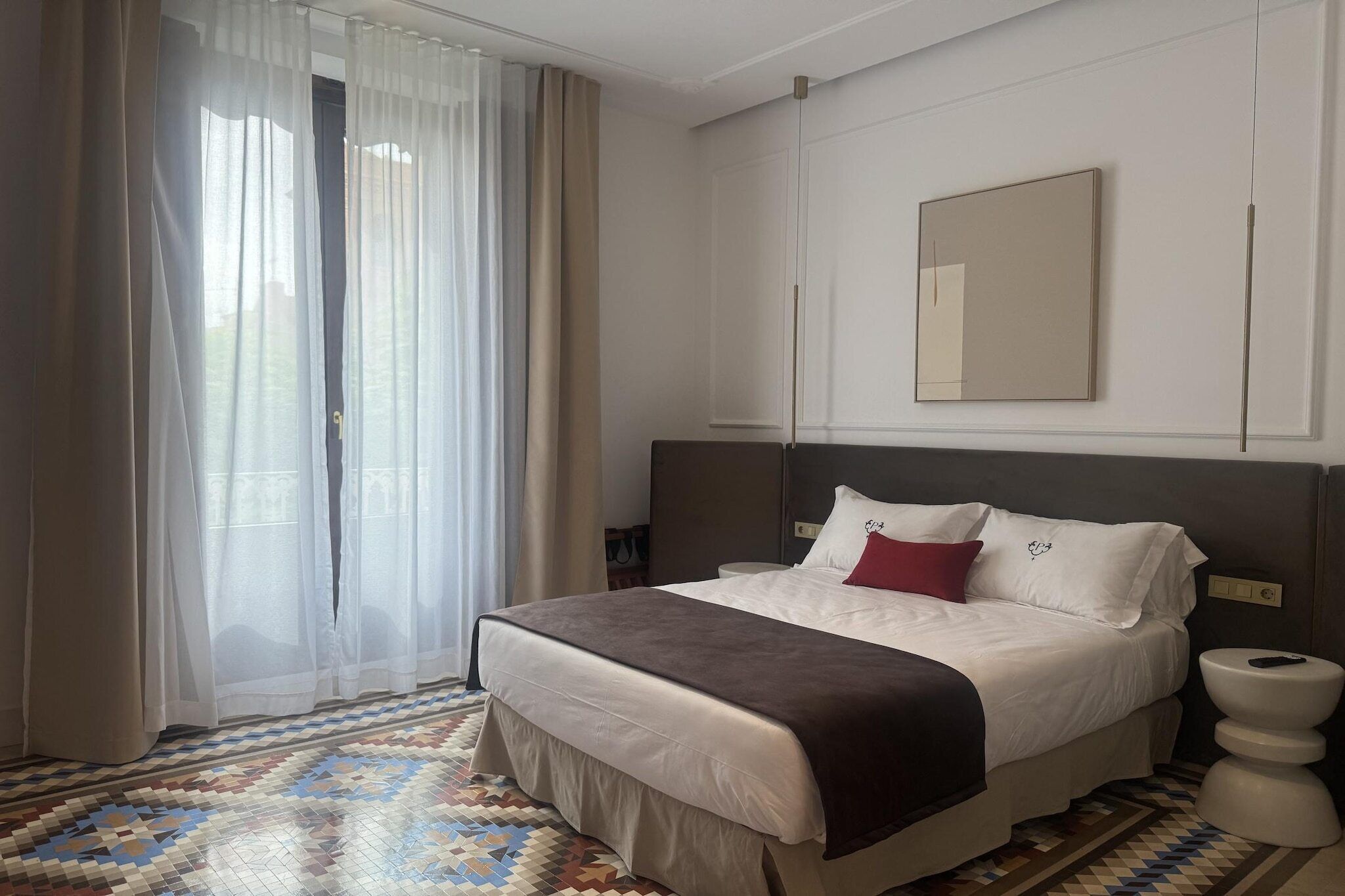 Habitación de hotel con cama, mesita de noche, inodoro y ventana con cortinas.