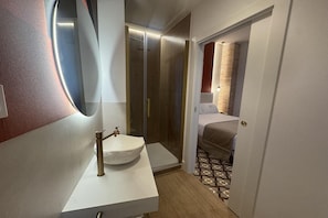 Un baño moderno con un lavabo redondo, un espejo y una zona de ducha.