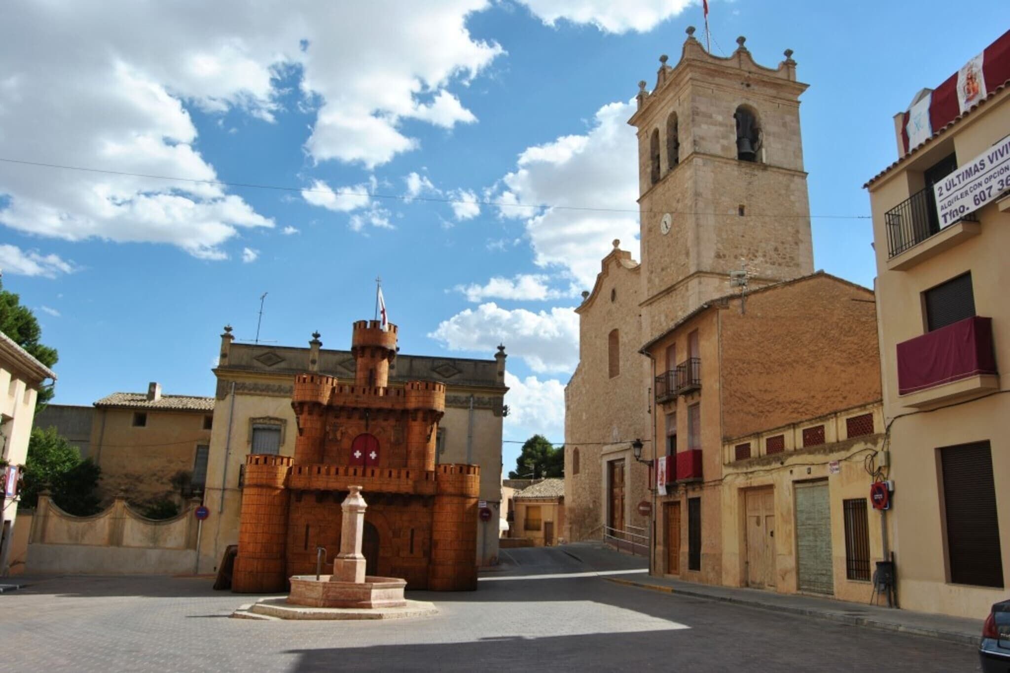 A historic town square with a prominent castle-like structure, a church with a bell tower, and traditional buildings.