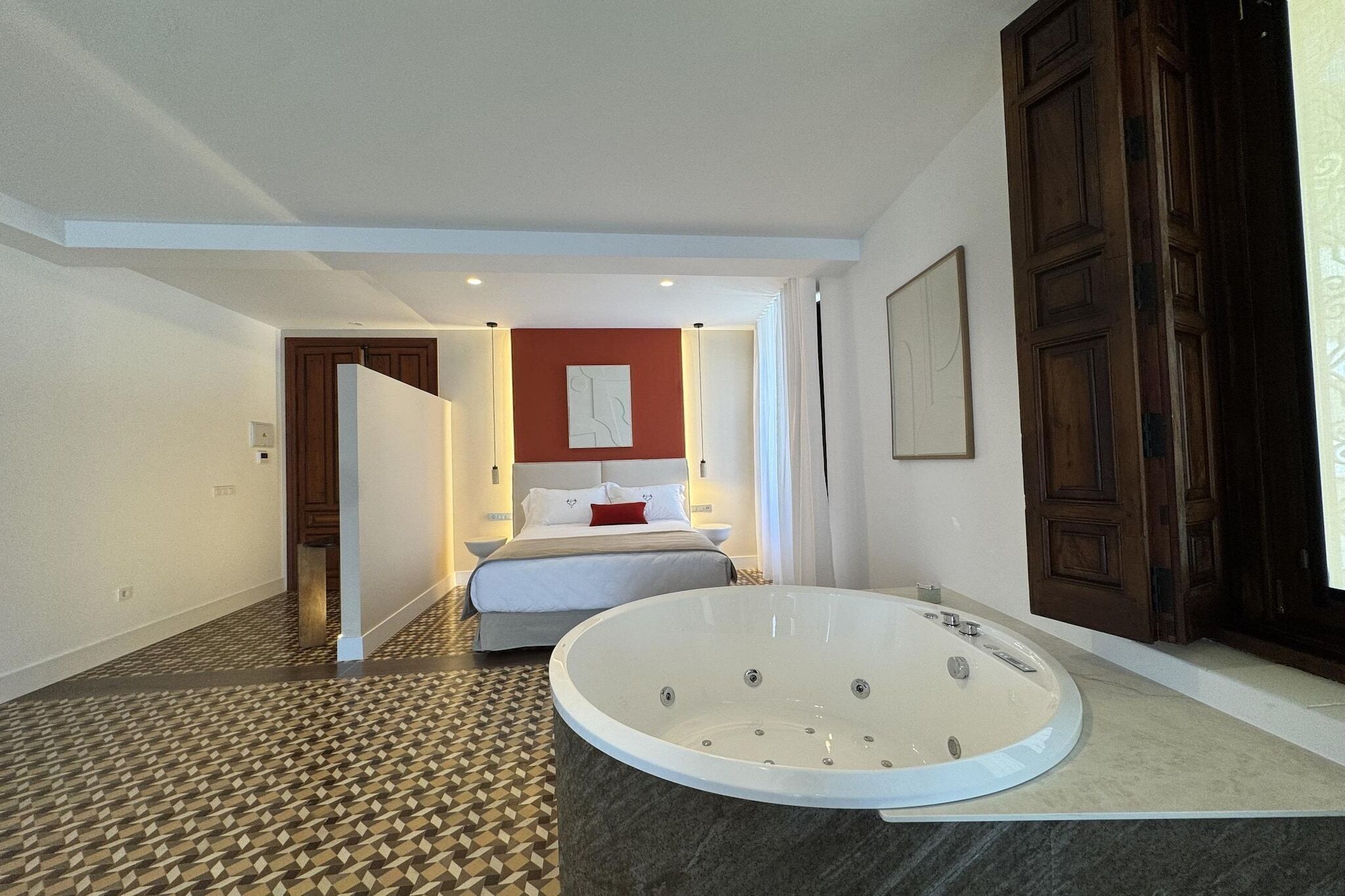 Habitación de hotel con una bañera grande, una cama y una pared decorada en rojo.