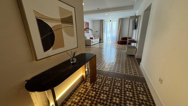 En hotellkorridor med ett rutmönstrat golv, ett modernt handfat och en stor, abstrakt målning på väggen.
