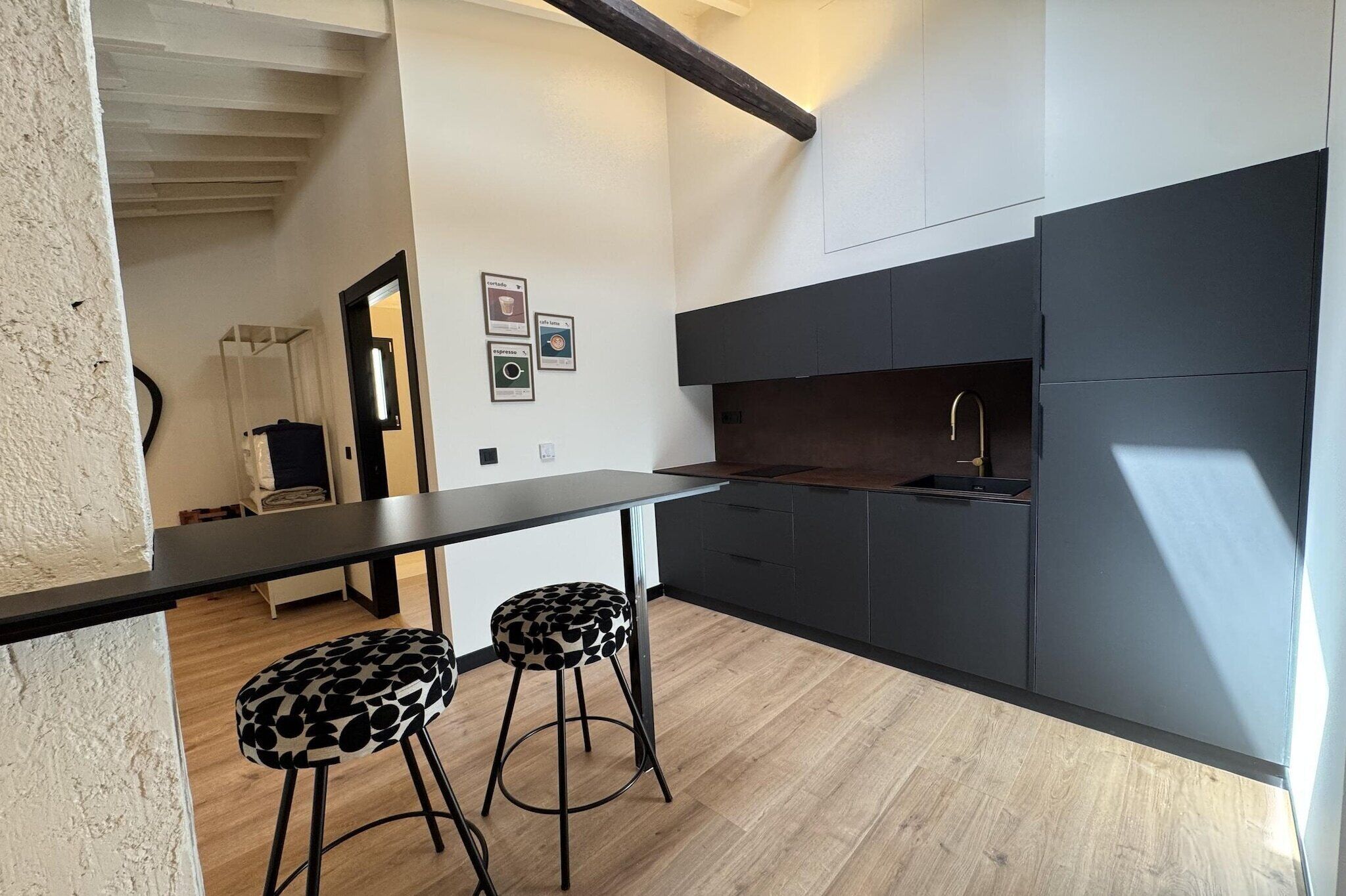 Une cuisine moderne avec un plan de travail noir, deux tabourets à motifs noir et blanc et un crédence de couleur sombre.
