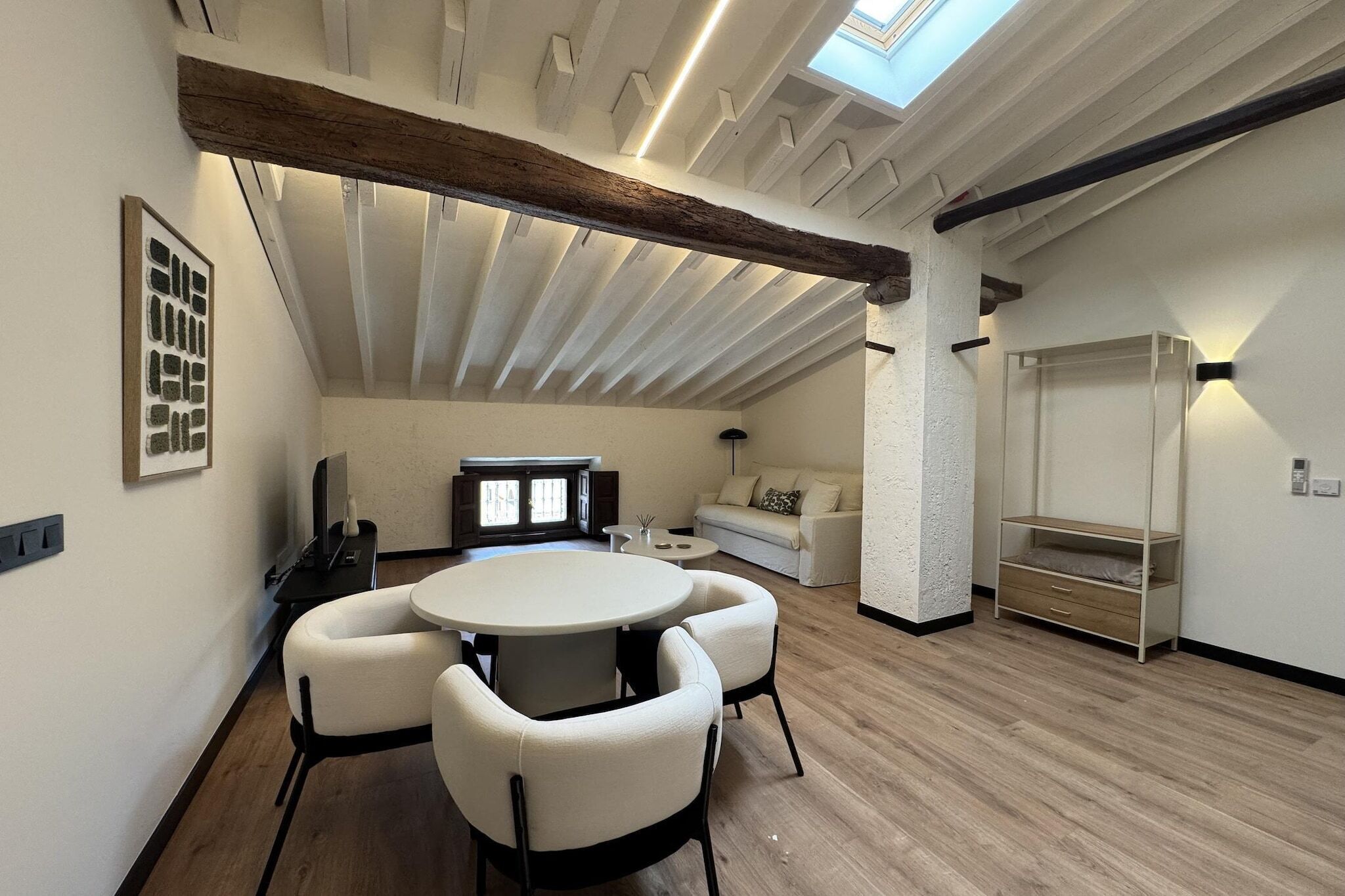 Une pièce spacieuse avec un plafond haut, une lucarne, une table ronde avec des chaises, un canapé et une bibliothèque intégrée.