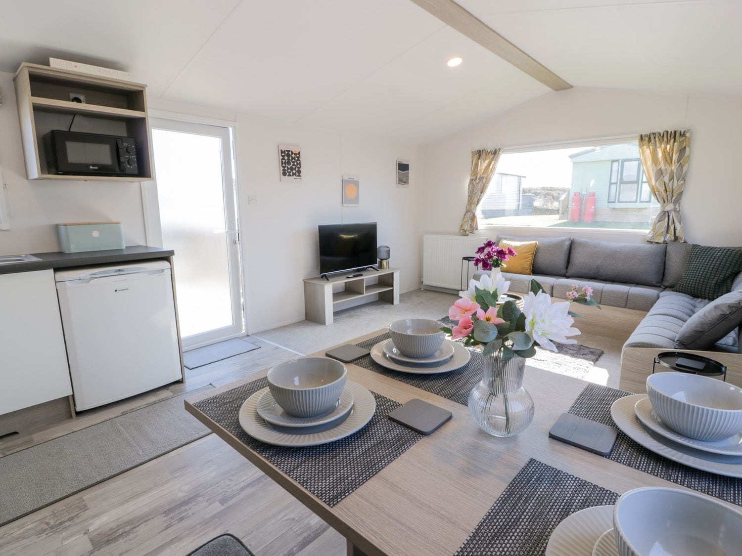 Una sala moderna con sofá, televisión, mesa de comedor con cuencos y una zona de cocina con microondas.