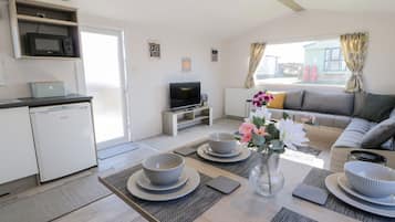 Una sala moderna con sofá, televisión, mesa de comedor con cuencos y una zona de cocina con microondas.