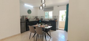A modern kitchen with a dining area, featuring a refrigerator, stove, sink, and a dining table set for four. - Le Coin Grenadier - 2BR Apartment (Flic en Flac)