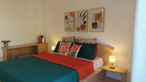 Ein Schlafzimmer mit einem Bett, Nachttischen, einem Schreibtisch und einer kleinen Pflanze.