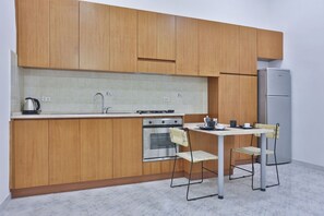 A compact kitchen with wooden cabinets, a stainless steel refrigerator, a gas stove, and a small dining table with two chairs. - A comfortable and large apartment ideal for four guests and strategically located in the heart of Naples, allowing you to fully experience the city's authentic atmosphere; it is just steps away from Piazza del Plebiscito and the entrance to the evocative (Napoli)