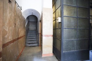 A narrow hallway with a staircase leading to a door with a metal grid. - A comfortable and large apartment ideal for four guests and strategically located in the heart of Naples, allowing you to fully experience the city's authentic atmosphere; it is just steps away from Piazza del Plebiscito and the entrance to the evocative (Napoli)